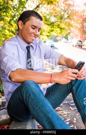 Smiling Mixed Race man sitting on curb texting on cell phone Banque D'Images