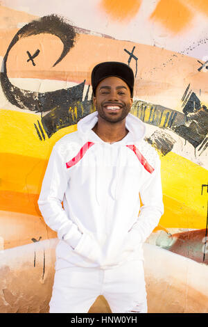 Smiling Black man leaning on wall graffiti Banque D'Images