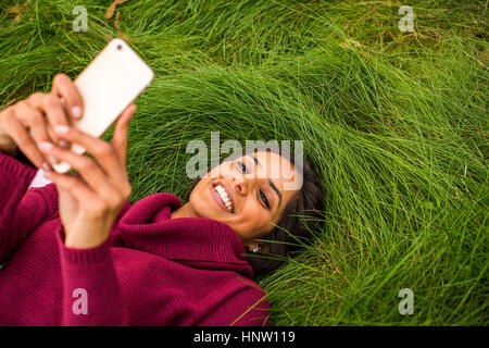 Smiling woman laying in grass texting on cell phone Banque D'Images