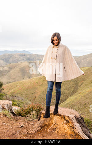 Smiling woman wearing poncho standing on tree stump Banque D'Images