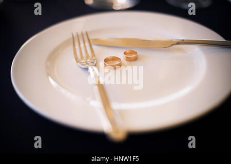 Deux anneaux de mariage se situent sur une plaque blanche à côté d'un couteau et fourchette Banque D'Images