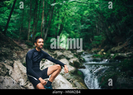 Portrait homme assis sur des rochers près de forest stream Banque D'Images