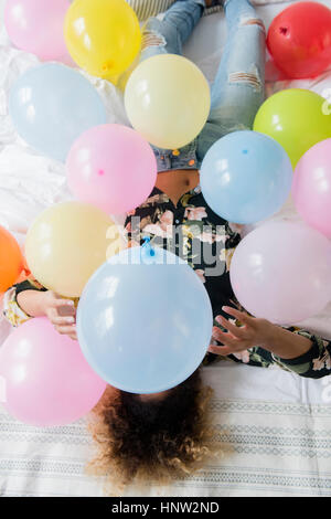 Mixed Race woman sitting on bed couverts avec des ballons Banque D'Images