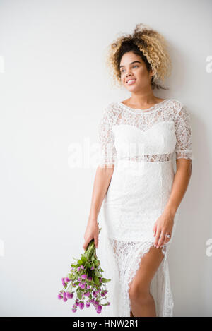 Mixed Race woman wearing wedding dress leaning on wall Banque D'Images