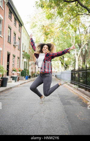 Mixed Race woman sauter de joie dans la ville Banque D'Images