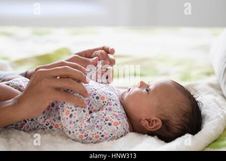 Hispanic mother holding hands with baby daughter on bed Banque D'Images