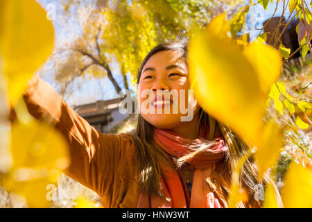 Smiling Asian Woman Reaching for leaf en automne Banque D'Images