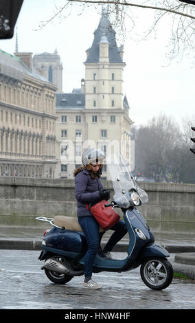 Une jeune femme vérifie son téléphone alors qu'elle attend à un ensemble de feux de circulation sur son Vespa scooter à poster Neuf, Paris. Banque D'Images