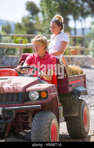 Les jeunes hommes et les femmes mariés roulant ramasser avec des bottes de paille dans les zones rurales d'équitation Banque D'Images