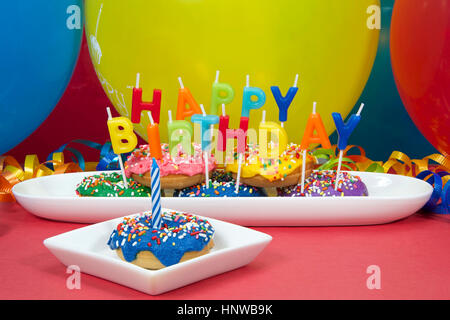 Beignet miniature gâteau pour première fête d'anniversaire. Multicolor donuts sur plaque blanche avec Joyeux Anniversaire bougies. Un beigne givré bleu cupcake on plate Banque D'Images