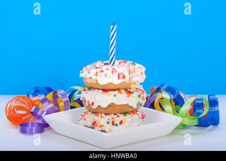 Beignet miniature gâteau pour première fête des beignets gâteau. avec glaçage buttercream et rainbow sprinkles sur plaque blanche avec une bougie bleue. Banque D'Images