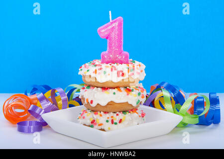 Beignet miniature gâteau pour première fête des beignets gâteau. avec glaçage buttercream et rainbow sprinkles sur plaque blanche avec une bougie rose. Banque D'Images