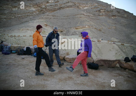 Gel Senior citizen randonneurs habillés dans le froid matin n'tai chi pour s'échauffer avant de démarrer une randonnée difficile. Makhtesh Ramon, Néguev, Israël. Banque D'Images