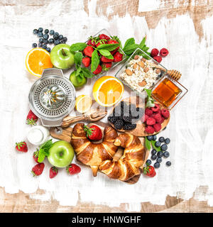 Concept d'aliments sains. Le petit-déjeuner avec croissants, céréales, fruits frais, fruits rouges, orange, pomme, lait. Vue d'en haut Banque D'Images