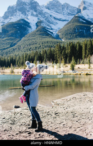 Mère et fille s'embrasser maintenant au bord de la rivière, trois soeurs, montagnes Rocheuses, Canmore, Alberta, Canada Banque D'Images