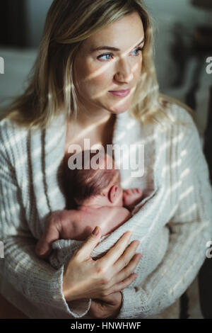 Portrait of mid adult woman berçant bébé nouveau-né fille enveloppé à Cardigan Banque D'Images