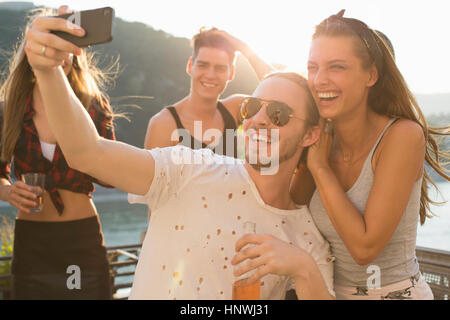 Jeune homme en tenant avec selfies amie au toit-terrasse au bord de l'eau partie, Budapest, Hongrie Banque D'Images