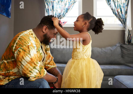 Fille en costume princesse tiara mise sur le père dans la salle de séjour Banque D'Images