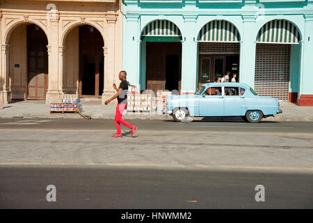 Un homme marche le long d'un cubain Havana street avec un classique des années 50 American car la conduite dans l'arrière-plan Banque D'Images