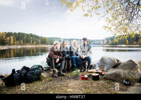 Amis assis sur Lakeshore pendant camping Banque D'Images