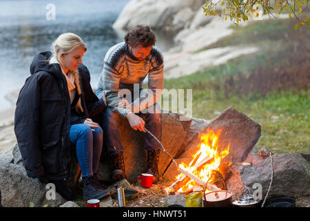 Couple sitting by campfire sur Lakeshore Banque D'Images
