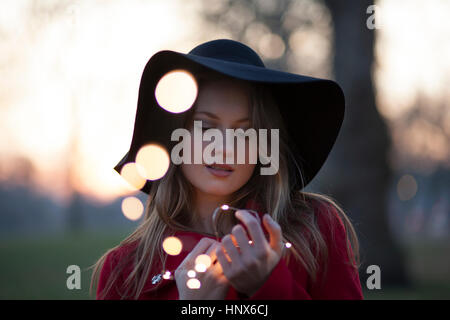 Jeune femme dans le parc à la recherche de lumières dans sa main, London, UK Banque D'Images