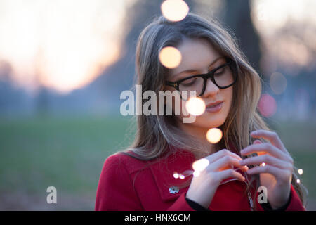 Jeune femme dans le parc à la recherche de lumières dans sa main, London, UK Banque D'Images