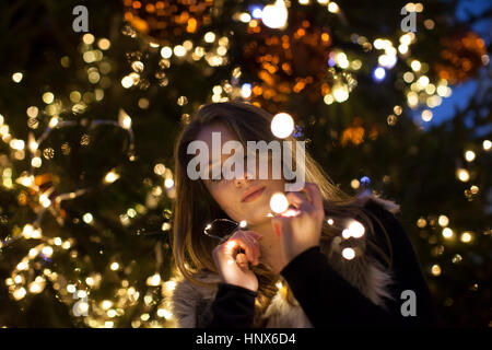 Jeune femme à la recherche de lumières dans sa main, d'arbres en arrière-plan Banque D'Images