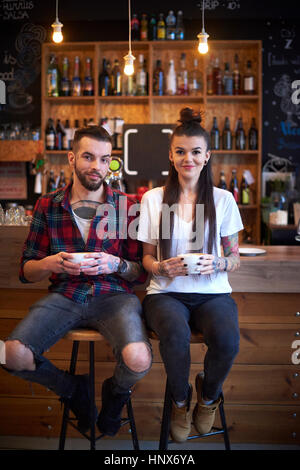 Couple assis côte à côte sur des tabourets dans cafe looking at camera smiling Banque D'Images