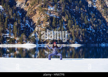 Femme dans les vêtements d'hiver la pratique du yoga présentent pour l'Autriche, au bord du lac enneigé Banque D'Images