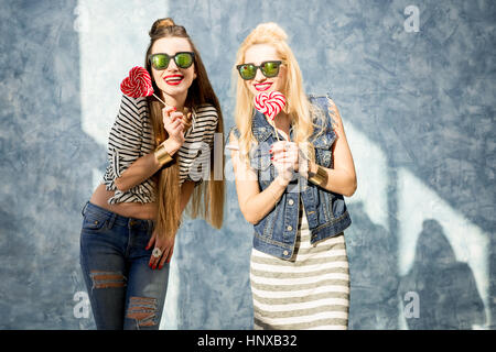 Young female friends having fun with bonbons debout sur le mur bleu Banque D'Images