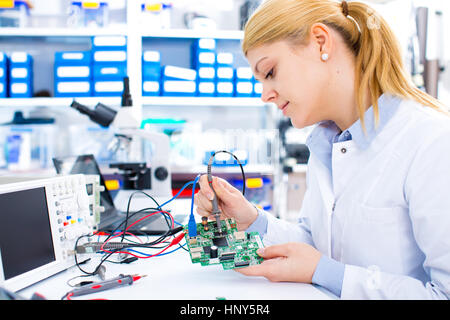 Ingénieur travaillant avec des circuits. Un ingénieur circuits soudures femme assis à une table. Usine de production de Microchip. Processus technologique. L'assemblage Banque D'Images