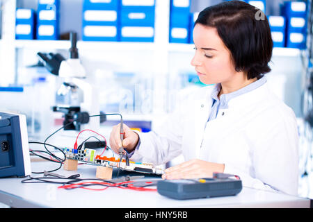 Ingénieur travaillant avec des circuits. Un ingénieur circuits soudures femme assis à une table. Usine de production de Microchip. Processus technologique. L'assemblage Banque D'Images