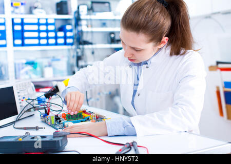 Ingénieur travaillant avec des circuits. Un ingénieur circuits soudures femme assis à une table. Usine de production de Microchip. Processus technologique. L'assemblage Banque D'Images