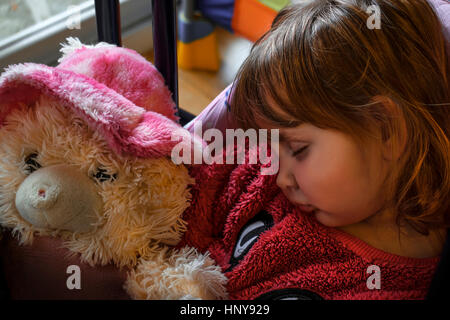 Petite fille blonde portant un chandail de fourrure rose endormie avec un ours en peluche dans ses mains. Banque D'Images