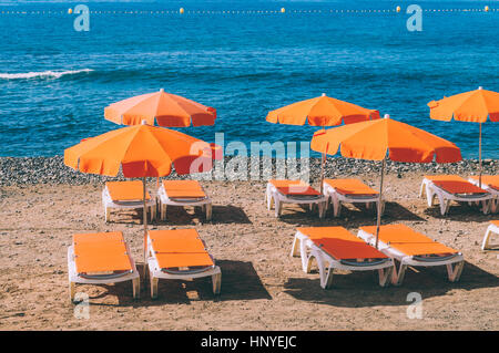 Parasols et transats Orange contre Stony Beach et l'océan Banque D'Images