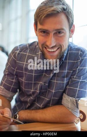 Homme assis dans un café avec carte de crédit en main, souriant gaiement Banque D'Images