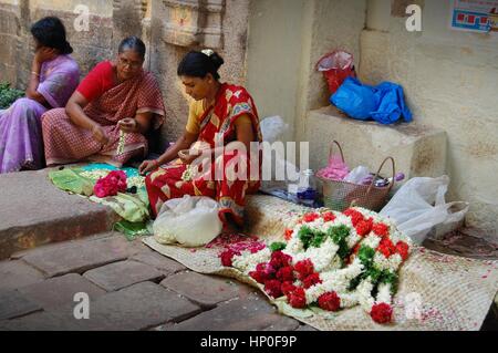 Femmes locales faisant des guirlandes de fleurs pour les festivaliers du temple au pied du rocher du Rhône, Tamil Nadu, Inde du Sud. Banque D'Images