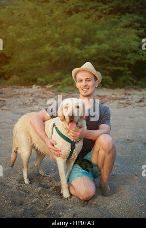 Homme avec chien labrador sable hugging on beach Banque D'Images