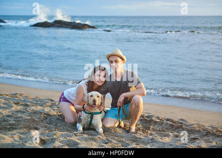 Couple avec chien labrador sable coucher du soleil sur la plage de l'océan Banque D'Images