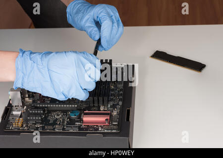 Close up of man mains avec des gants de l'installation de modules de mémoire DDR4 RAM dans l'emplacement sur la carte mère. Banque D'Images
