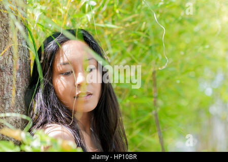 Woman leaning against tree trunk, regardant vers le bas dans la pensée Banque D'Images