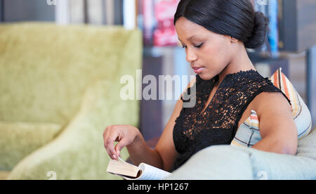 Femme africaine en tournant la page dans son livre assis sur canapé Banque D'Images