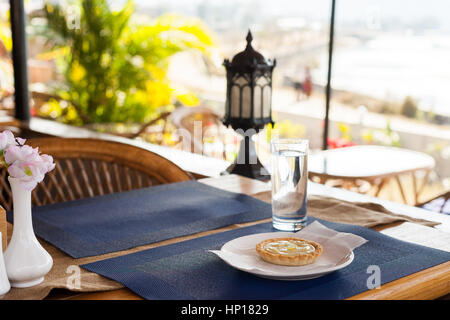 Tarte au citron avec de la crème anglaise le remplissage et les tranches de citron sur une plaque blanche, bleu mat et bois cafe table Banque D'Images