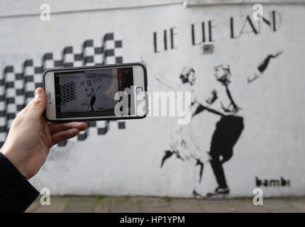 Un homme prend une photo d'un morceau de l'art de rue par l'artiste Bambi, intitulé mentir mentir Land - représentant le premier ministre Theresa mai et le président américain, Donald Trump, dansant dans une pose parodiant le film La La Land - à Islington, Londres. Banque D'Images