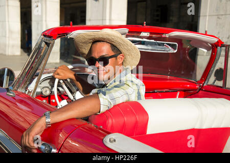 Voiture américaine rouge classique des années 1950 avec un homme cubain portant un chapeau de cow-boy assis dans le siège du conducteur regardant souriant à la caméra à la Havane Cuba Banque D'Images