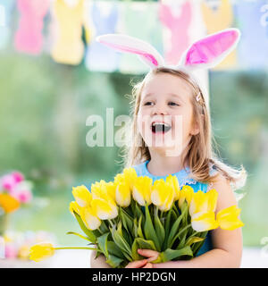 Happy little girl in Bunny Ears holding tulip fleurs''. Les enfants font la fête de Pâques. Les enfants s'amusant sur la chasse aux œufs de Pâques. Décoration maison, pastel b Banque D'Images