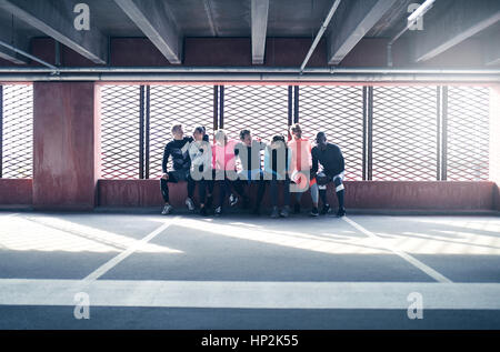 Groupe de jeunes adultes au sportif sportswear assis ensemble et rire de terrain contre la fenêtre. Banque D'Images