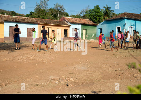 Un groupe de jeunes garçons cubains jouant au football sur un terrain difficile à Trinidad Cuba avec des logements traditionnels pauvres de Trinidad derrière Banque D'Images