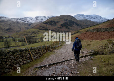 Lone Walker sur la façon de Cumbrie en Mickleden la vallée avec les montagnes de Wainwright Crinkle Crags & Bowfell dans la neige, Langdale, Lake District. Banque D'Images